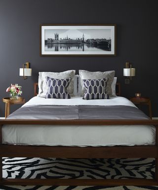 A bedroom with black walls, white and grey bedding, and a black and white graphic rug