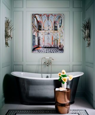 bathroom with pale aqua paneled walls, dark gray metallic slipper tub, copper table and colorful artwork