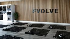 An empty Pvolve studio, with Pvolve mats and equipment laid out and black Pvolve signage mounted on a wooden wall.