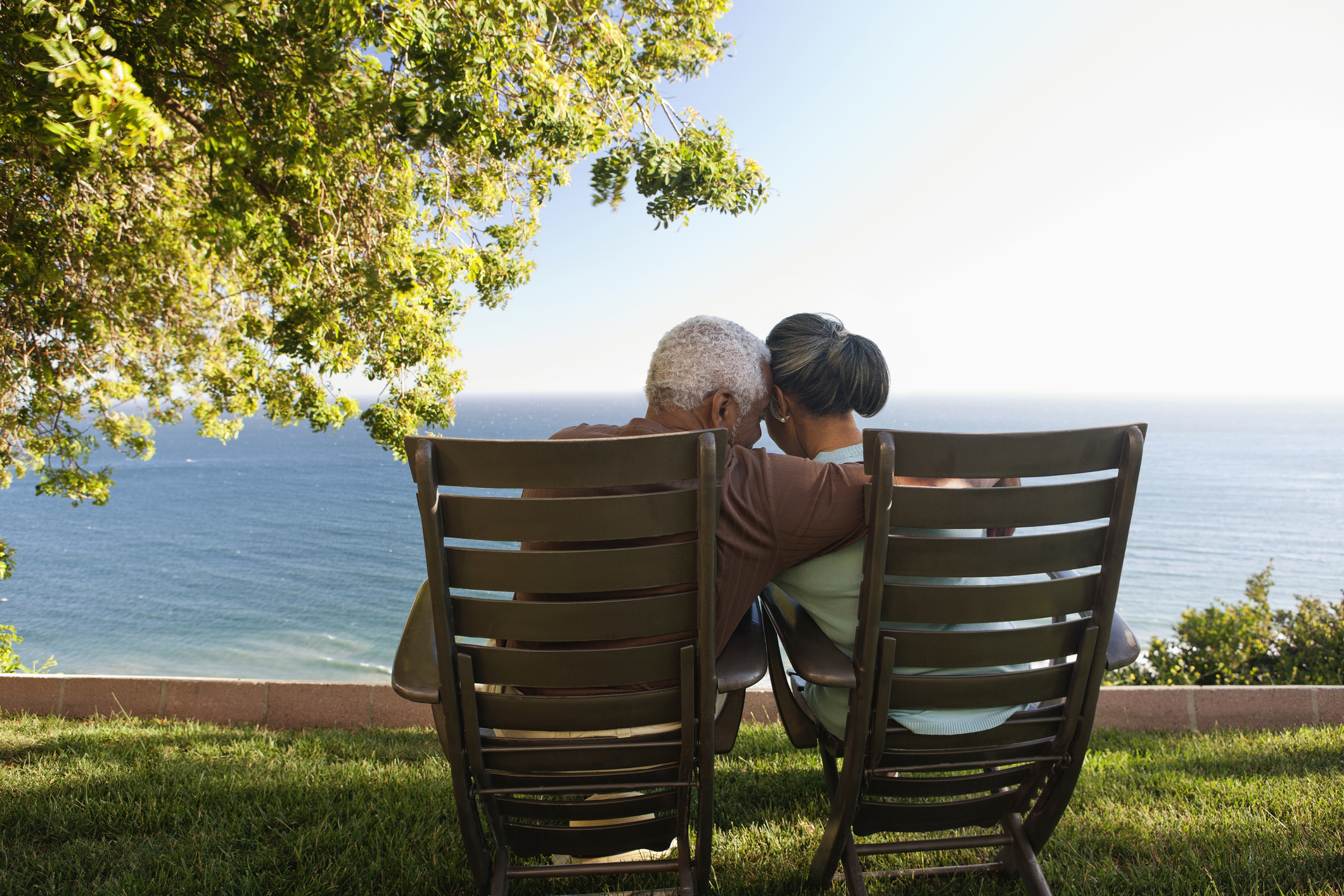 Senior couple hugging in lounge chairs on grass overlooking ocean