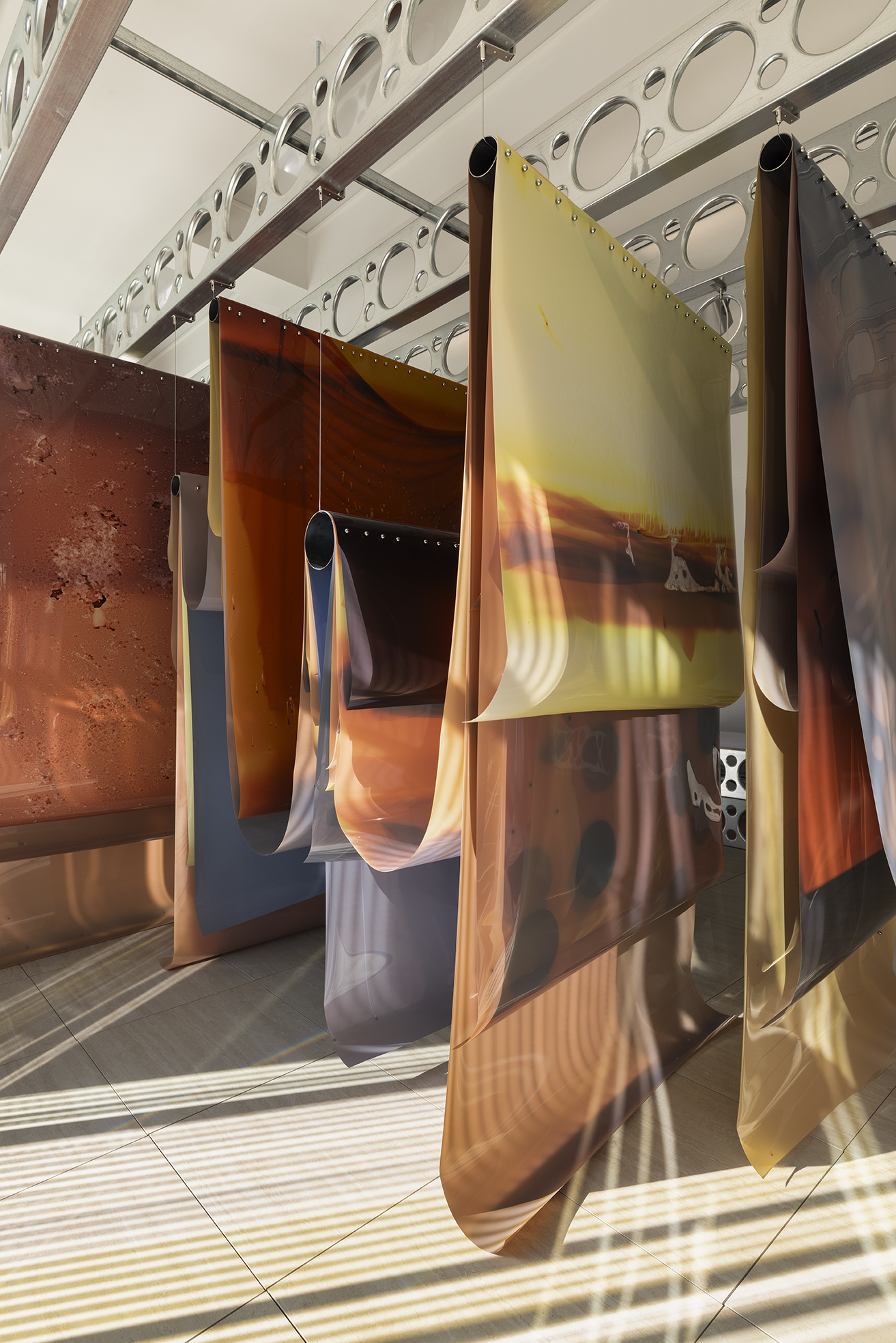 Long sheets of amber and yellow film hang in folds from perforated steel joists