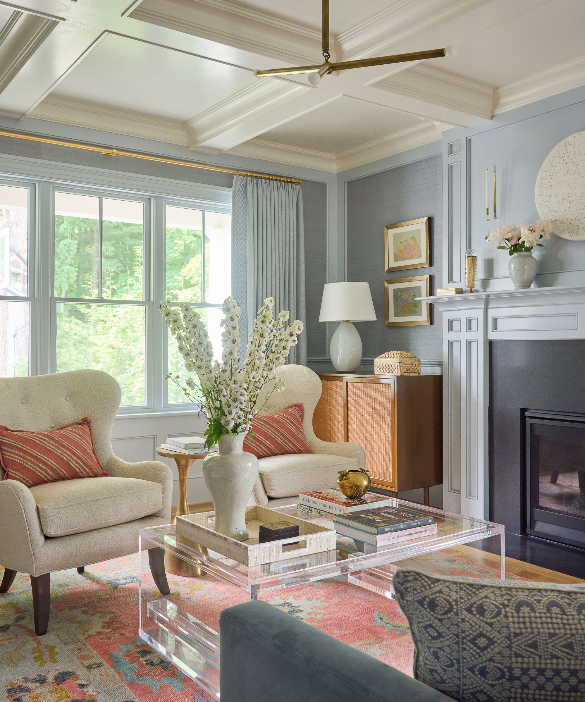 Living room with pale blue grasscloth walls, fireplace, cream armchairs, peach rug and lucite coffee table