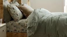 Layered bedscape featuring a burl wood frame, floral sheets, and a moss green ruffle velvet duvet 