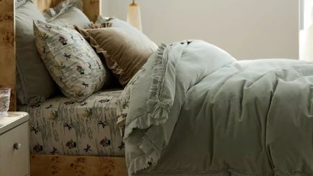Layered bedscape featuring a burl wood frame, floral sheets, and a moss green ruffle velvet duvet 