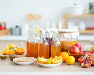 Collection of jars and bottles filled with colourful juice, surrounded by chopped and unchopped fruit in a clean kitchen