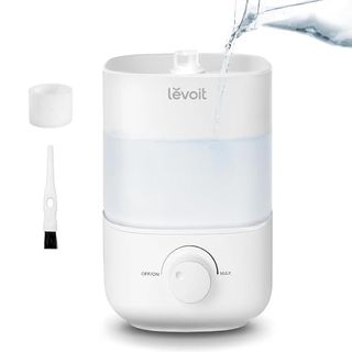 A small white humidifier with Levoit branding, water being poured into the top. Dial control front