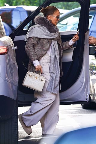 Jennifer Lopez wearing a tweed coat and khaki pants and looking at her phone