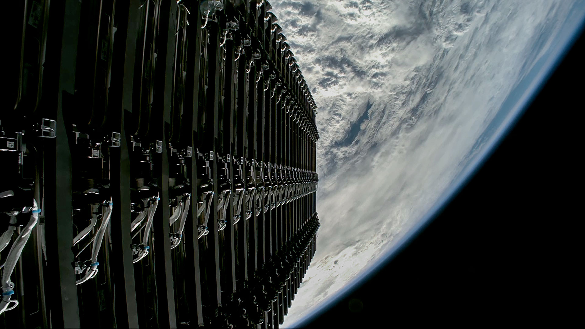 A stacked group of satellites is seen just before their deploy into orbit above a blue and white Earth.