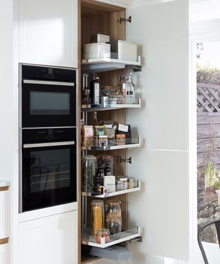 A custom-built pantry with pull-out shelving design in a modern kitchen with double oven
