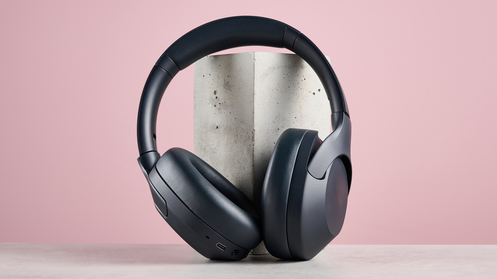 Tribit QuietPlus 81 leaning against block on pink background