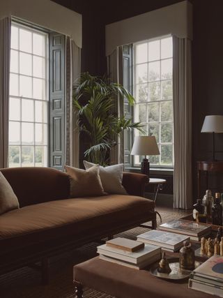 A brown living room with tall windows