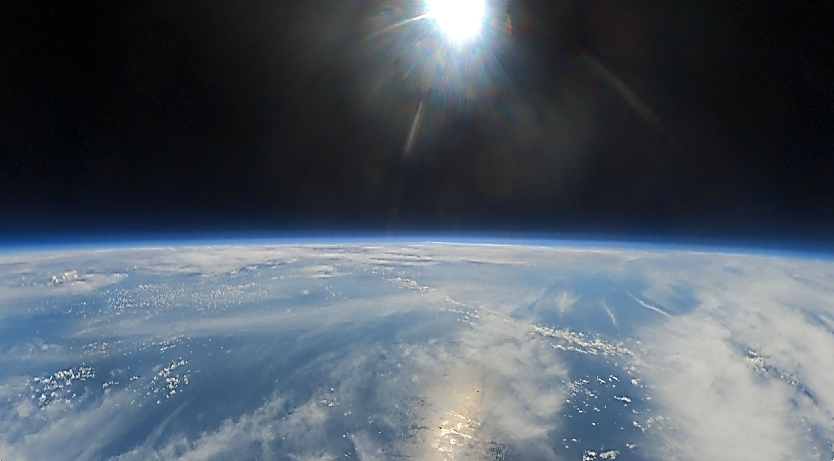 A view of a cure of earth at high altitude against a black sky with a glaring sun peaking out from the top near the center.