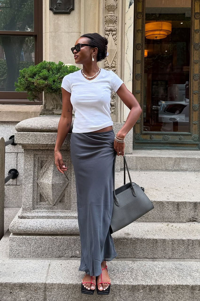 A woman wearing a white V-neck, gray skirt, and gray bag