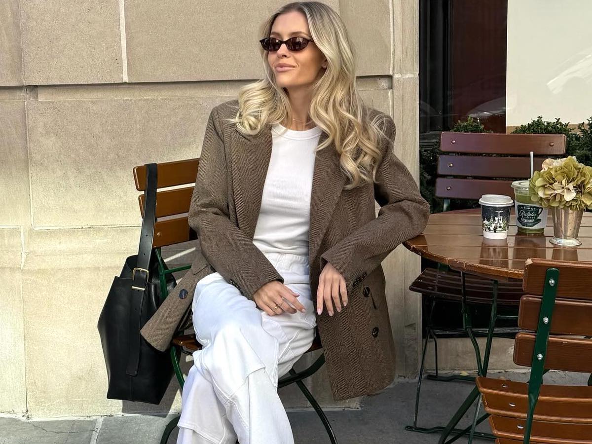style influencer Fredrika Ekerot sitting in a seat at an outdoor cafe in NYC wearing a brown blazer, white t-shirt, white pants, and black shoulder bag