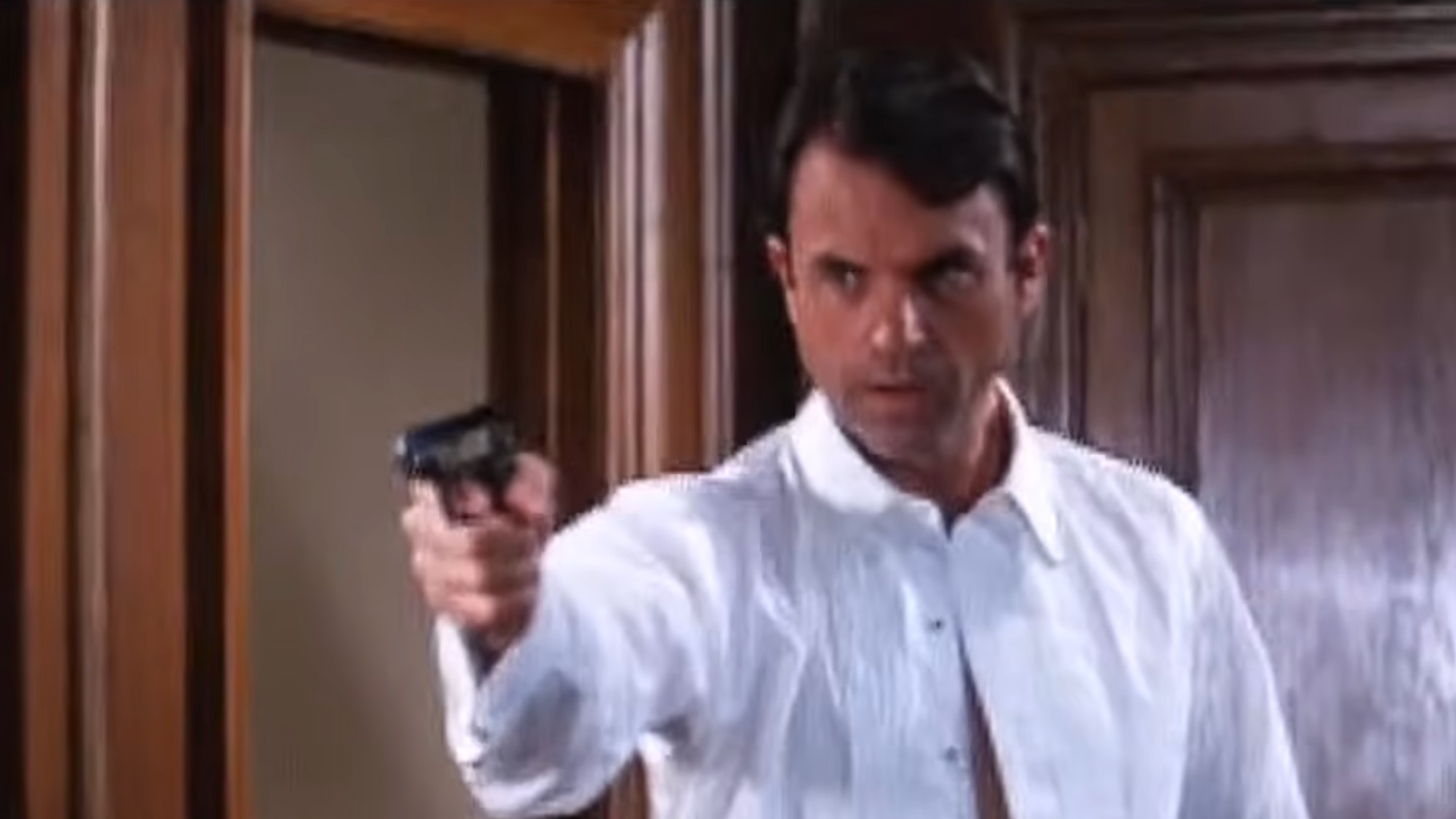Sam Neill in a white shirt, holding a Walther PPK in a screentest for James Bond