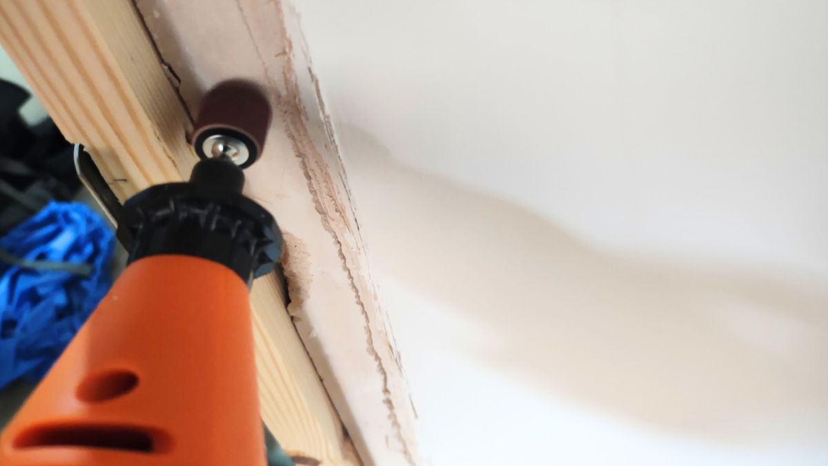 An orange rotary multi tool being used to remove old paint from a door frame