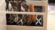 An expanding stainless steel pot lid organizer in a kitchen drawer with pan lids stacked inside. 