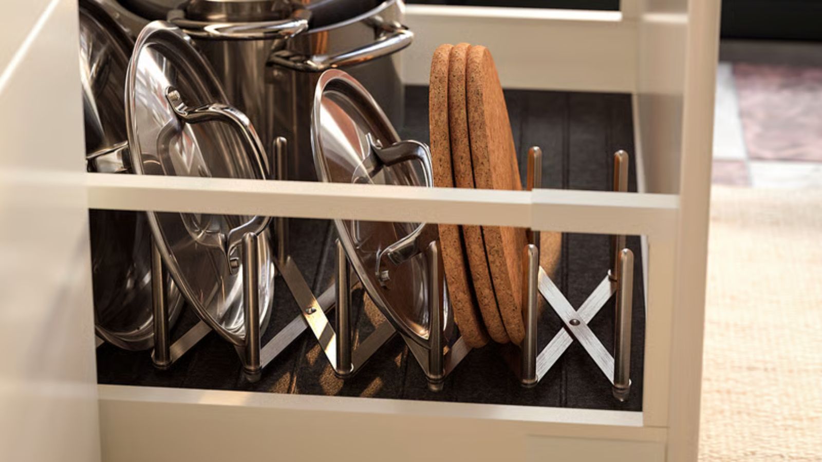 An expanding stainless steel pot lid organizer in a kitchen drawer with pan lids stacked inside. 