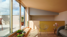 An extension space with sloped ceiling painted in warm joyful tones with sliding doors, a step to the outside space with plants on it and a mesh metal chair next to a small table with flowers