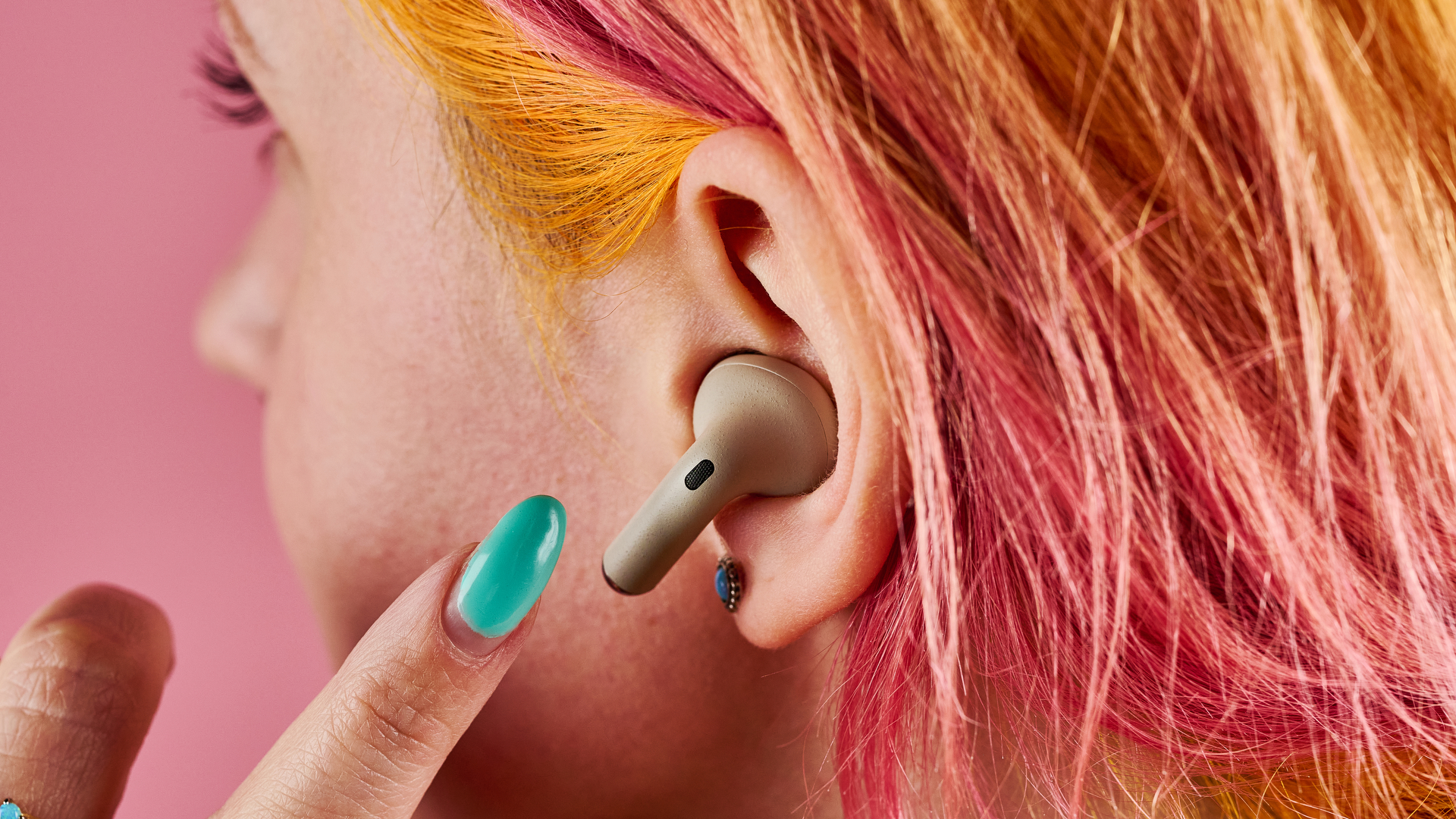 A close up side profile of a woman with orange and pink hair, she has one of the Motorola Moto Plus earbuds in her ear, and her finger is hovering ready to press the touch control area.