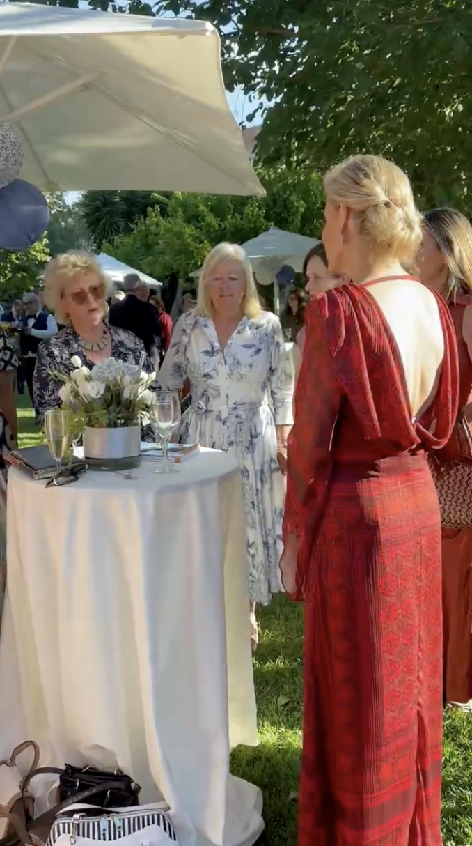 Duchess Sophie wearing a low-backed red dress talking to women at a garden party
