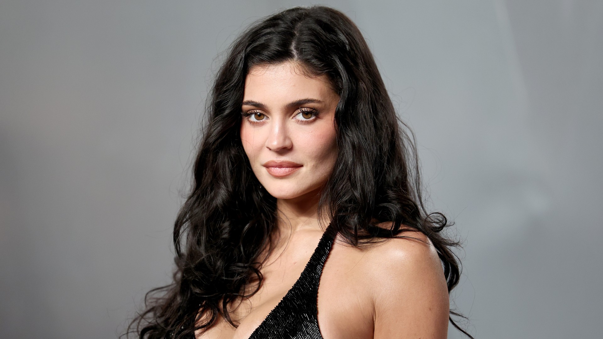 a white woman with long, dark hair photographed in front of a gray backdrop