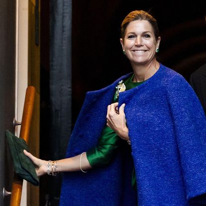 Queen Maxima wearing a blue coat holding a green clutch and smiling