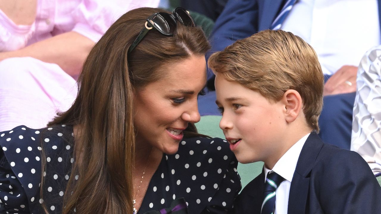 Prince George wearing a blue suit leaning over and talking to mom Kate Middleton, wearing a blue polka dot dress, at Wimbledon 2022