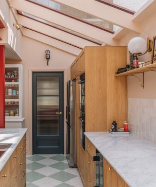 pink kitchen with green and ivory floor tiles, wood cabinets, marble countertops, open shelving, extension