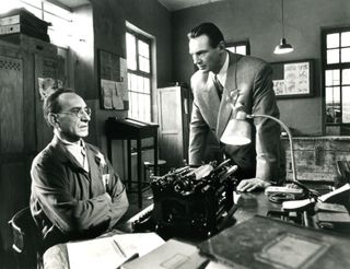 ralph fiennes and liam neeson talk in an office in a black and white still from Schindler's List