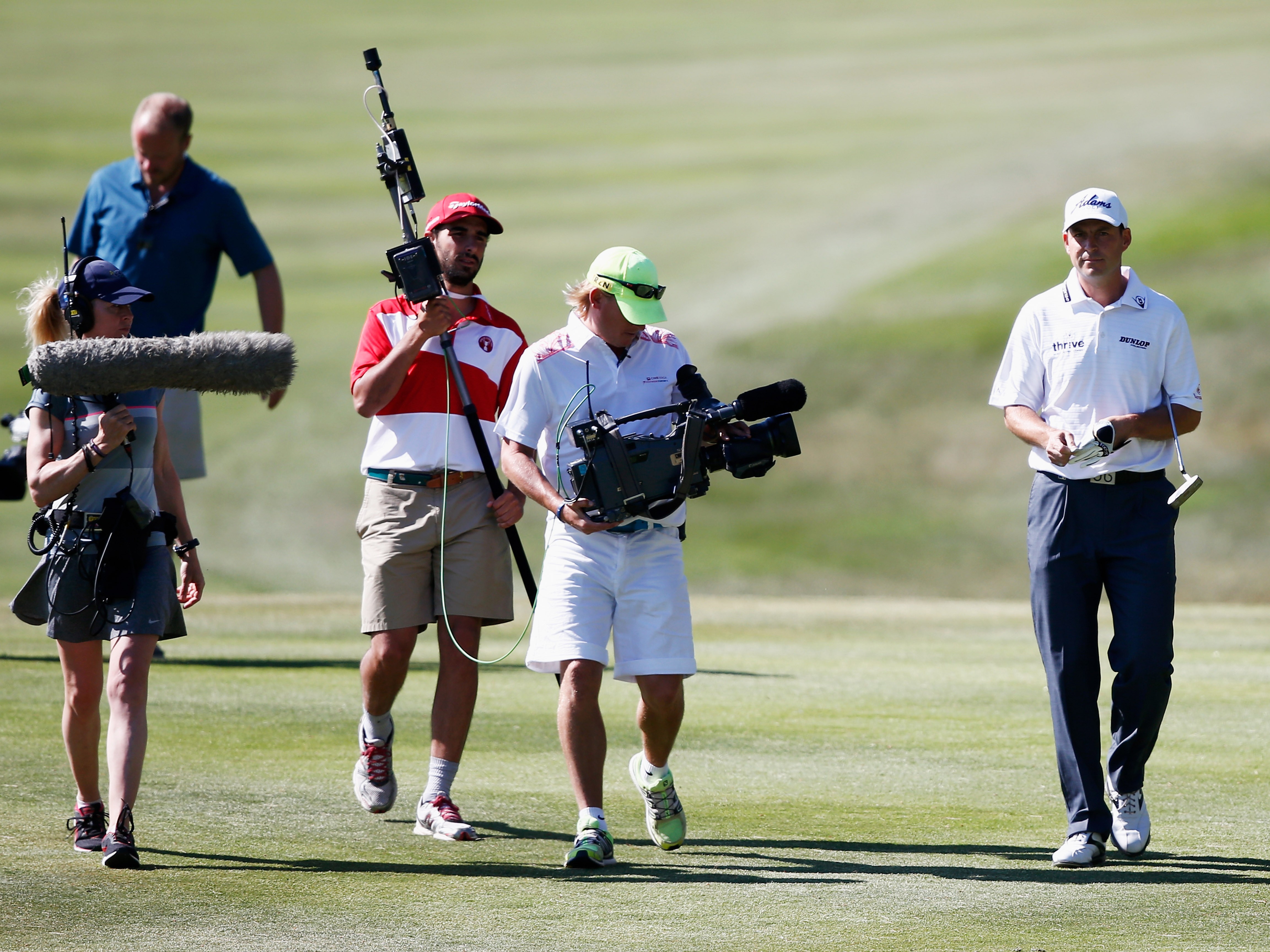 David Howell walks down a fairway accompanied by a camera of three walking alongside filming him walk
