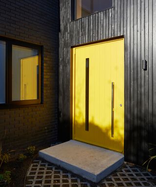 Black cladded house with bright yellow front door
