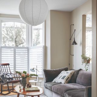 A bright living room with a grey velvet sofa, a paper lantern ceiling light, an adjustable wall light and a task table lamp on the side table