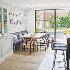 Open plan kitchen and dining area with a dining room table and bench seating, looking out into a garden