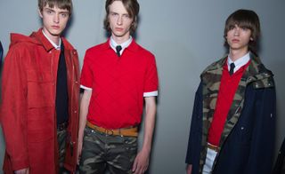 Three male models wearing clothing by Dior Homme in red and brown shades.