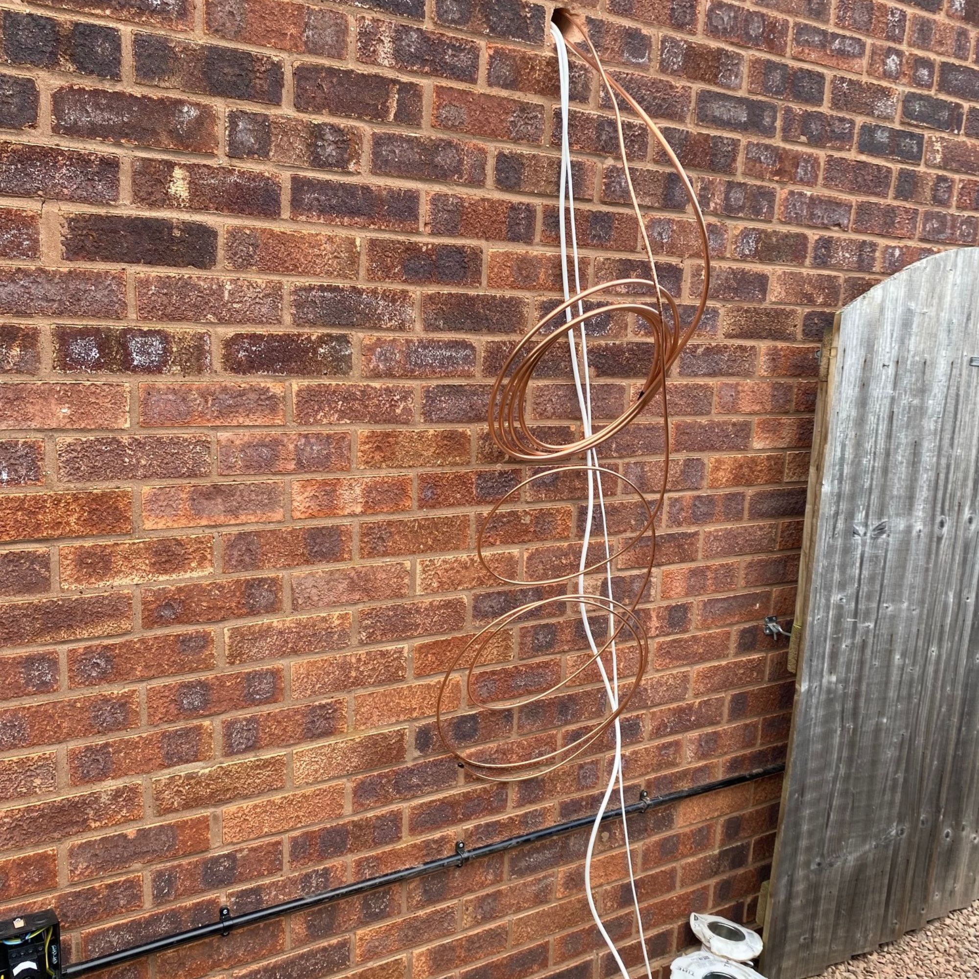 Cabling and pipework threaded outside through a hole in the wall ready to be connected to the outdoor air con unit