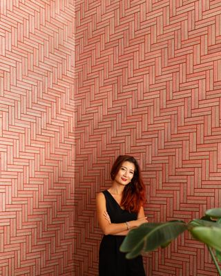 Elaine Yan Ling Ng is photographed next to the wall of tiles in a rectangle shape, in a beige and pink hue.