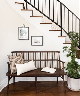A staircase area with white painted walls, dark wooden railings, matching wooden bench and wall art