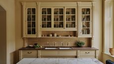 Yellow kitchen cabinets with subway tiled backsplash, wooden countertops and marble island