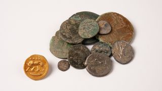 a pile of rusted and worn coins sits to the right of a clean, golden coin with a four legged animal etched into it