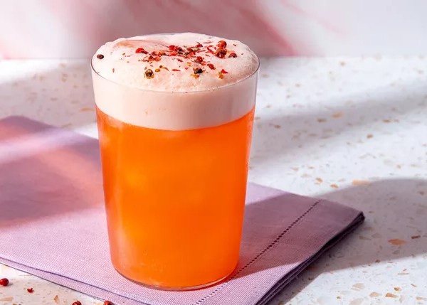 an orange drink with a froth in a tumbler on a mauve napkin