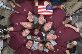 The 10 combined crewmembers of STS-135 and Expedition 28 pose with the STS-1 flag aboard the International Space Station. The flag flew on NASA's first shuttle mission in 1981, and the final flight STS-135 in July 2011.