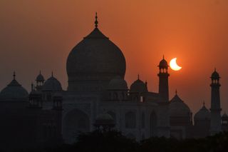 Partially eclipsed sun shines next to the Taj Mahal.