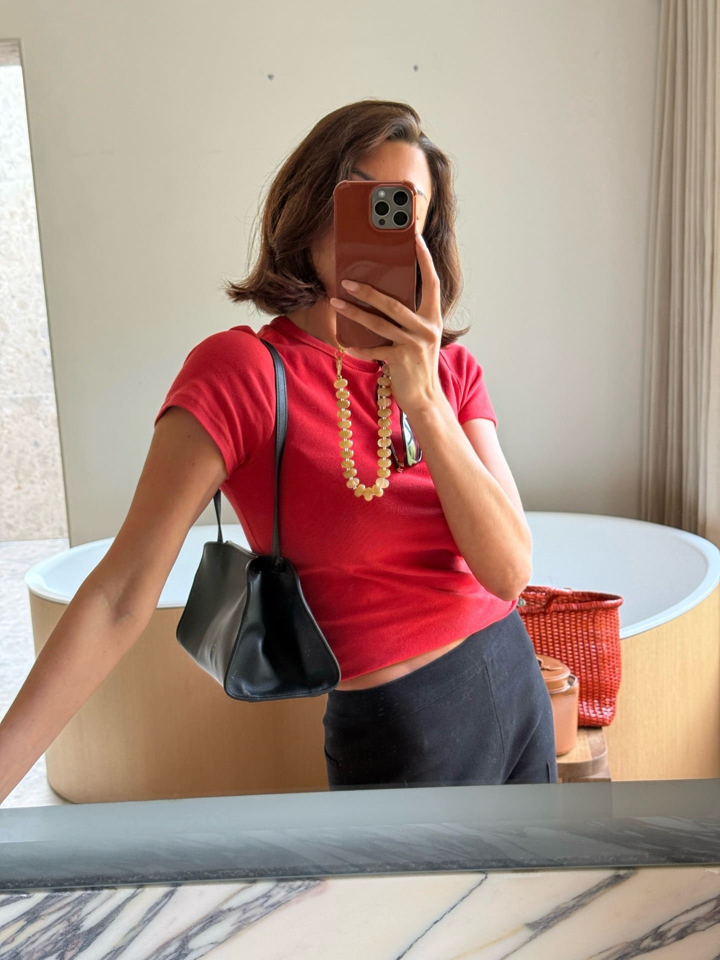 Influencer takes a mirror selfie wearing a red t-shirt with a black shoulder bag.