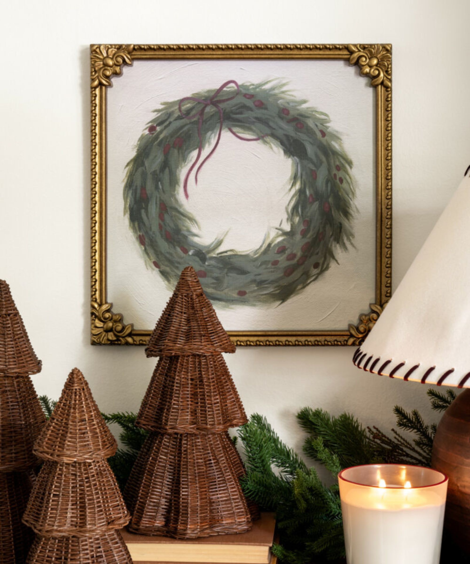Mantel with rattan christmas trees, gold frame with wreath and lit candle