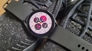 A black Samsung Galaxy Watch 4 laid across some black trainers