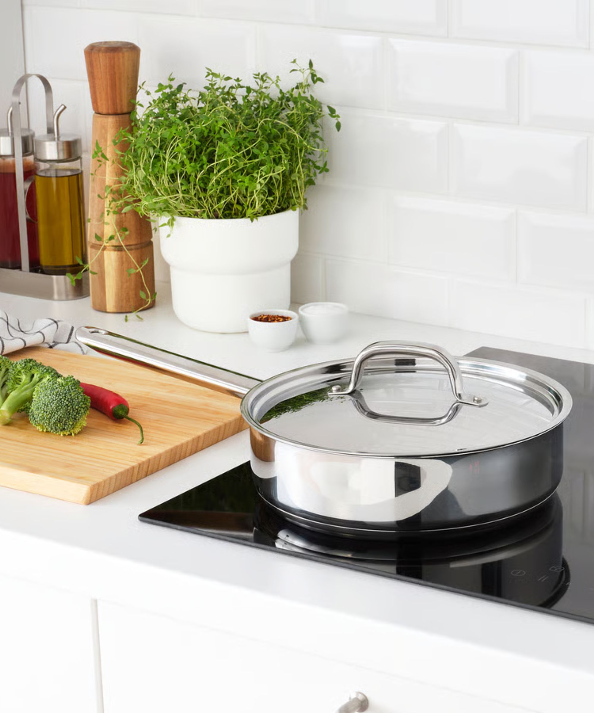 A stainless steel saut&amp;eacute; pan with a long handle and matching lid on a black electric stove top.
