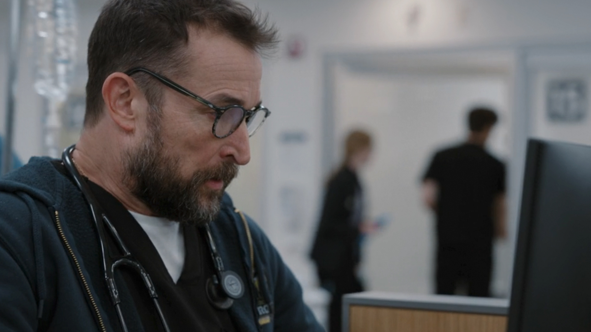Noah Wyle wearing glasses, looking at a computer in The Pitt
