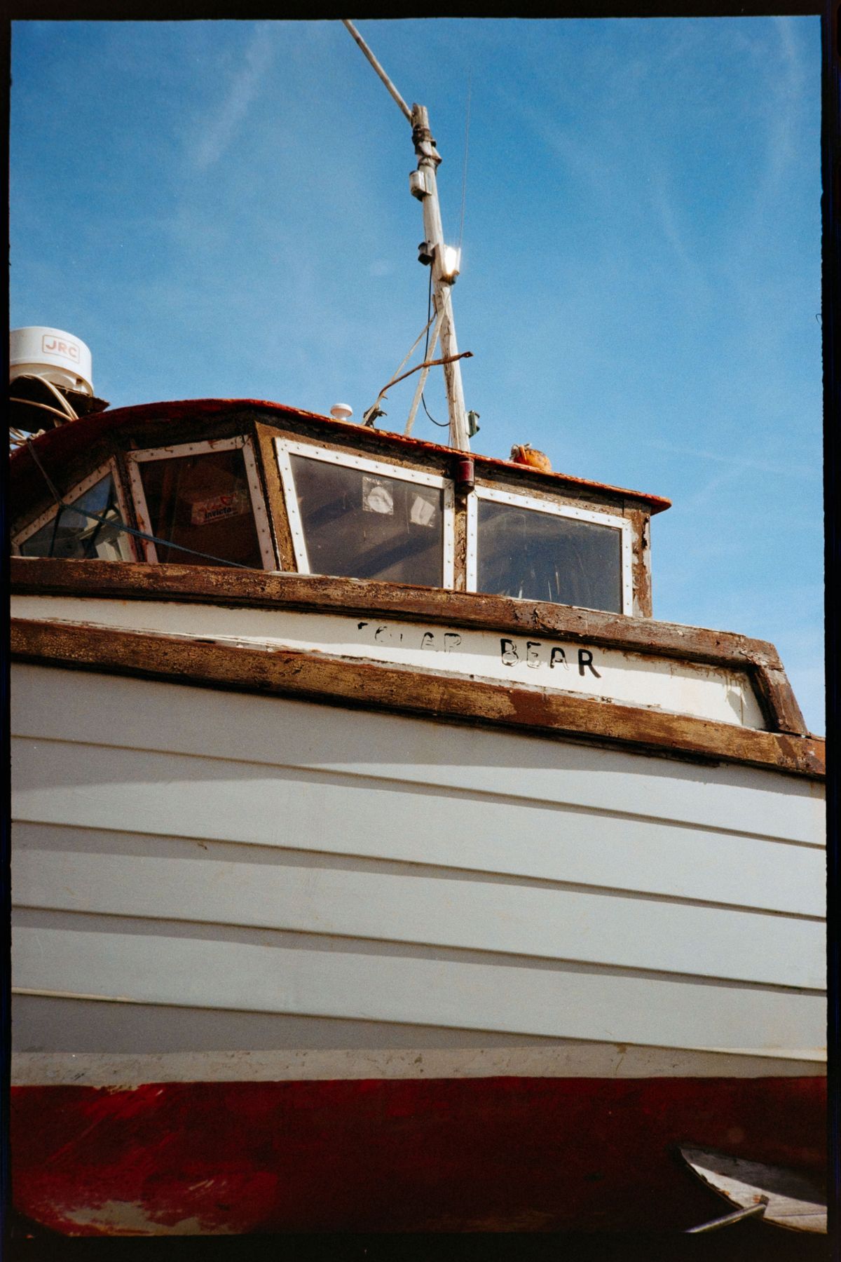 A close-up of an old fishing boat with weathered wood, peeling paint, and a blue sky behind it.