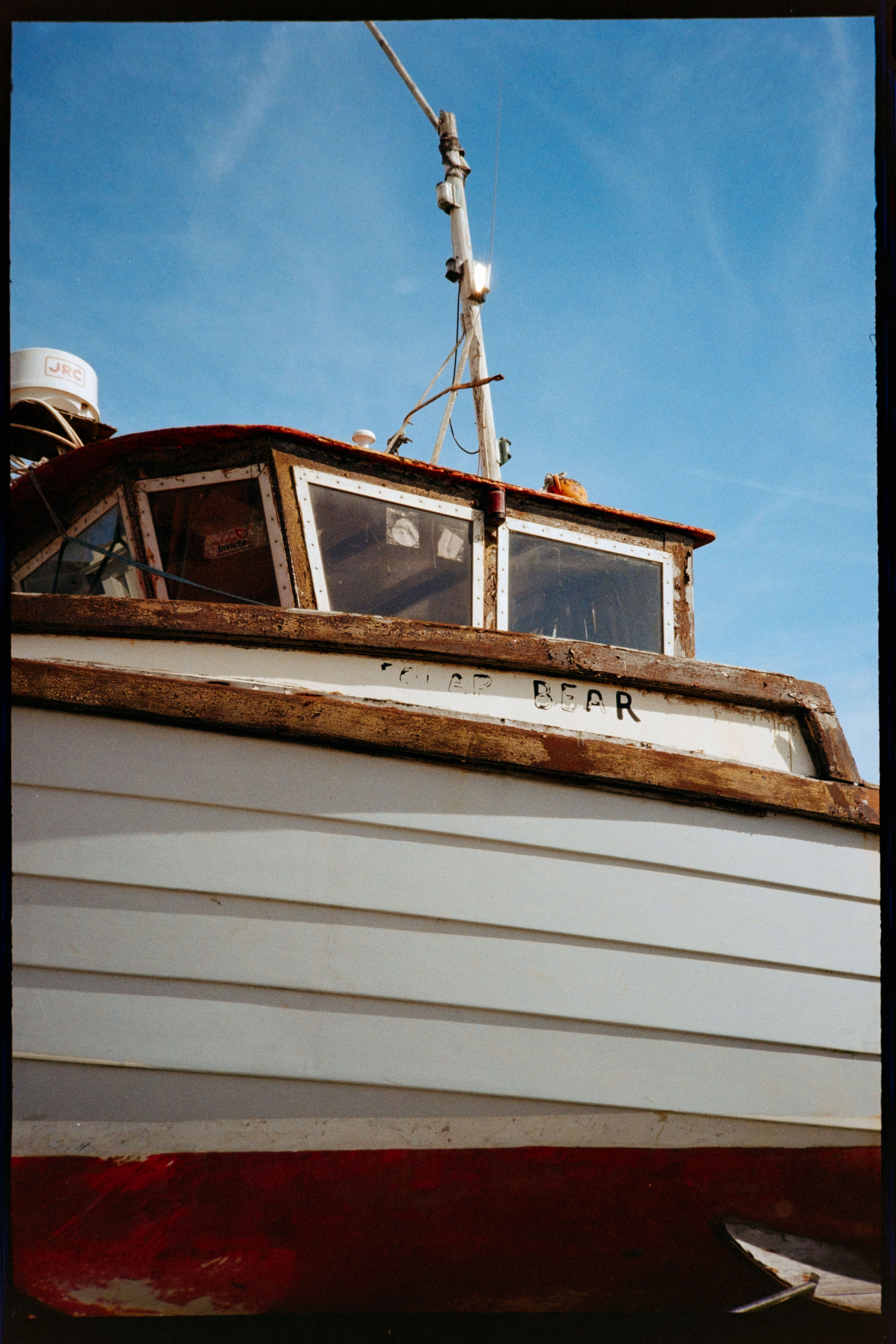 A close-up of an old fishing boat with weathered wood, peeling paint, and a blue sky behind it.